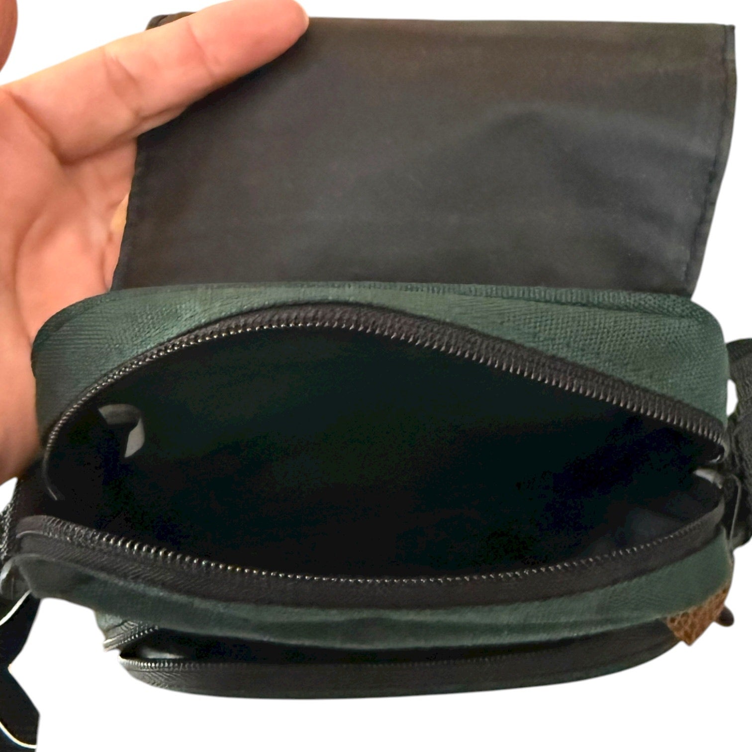 Green bag with a zipper being held open by a hand on a white background