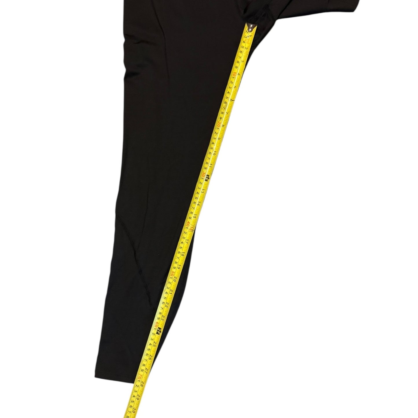 A close-up of a black garment leg with a yellow measuring tape running down the side to show the length, on a plain white background.