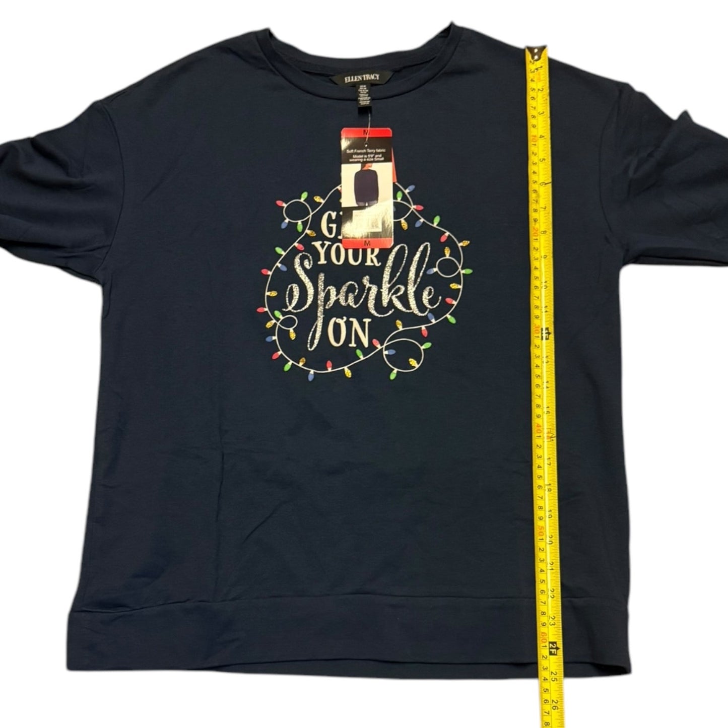 Blue shirt with 'Turn Your Sparkle On' text and Christmas lights design, with a measuring tape on a white background.