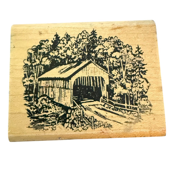 Wooden stamp with a design of a covered bridge and trees on a white background
