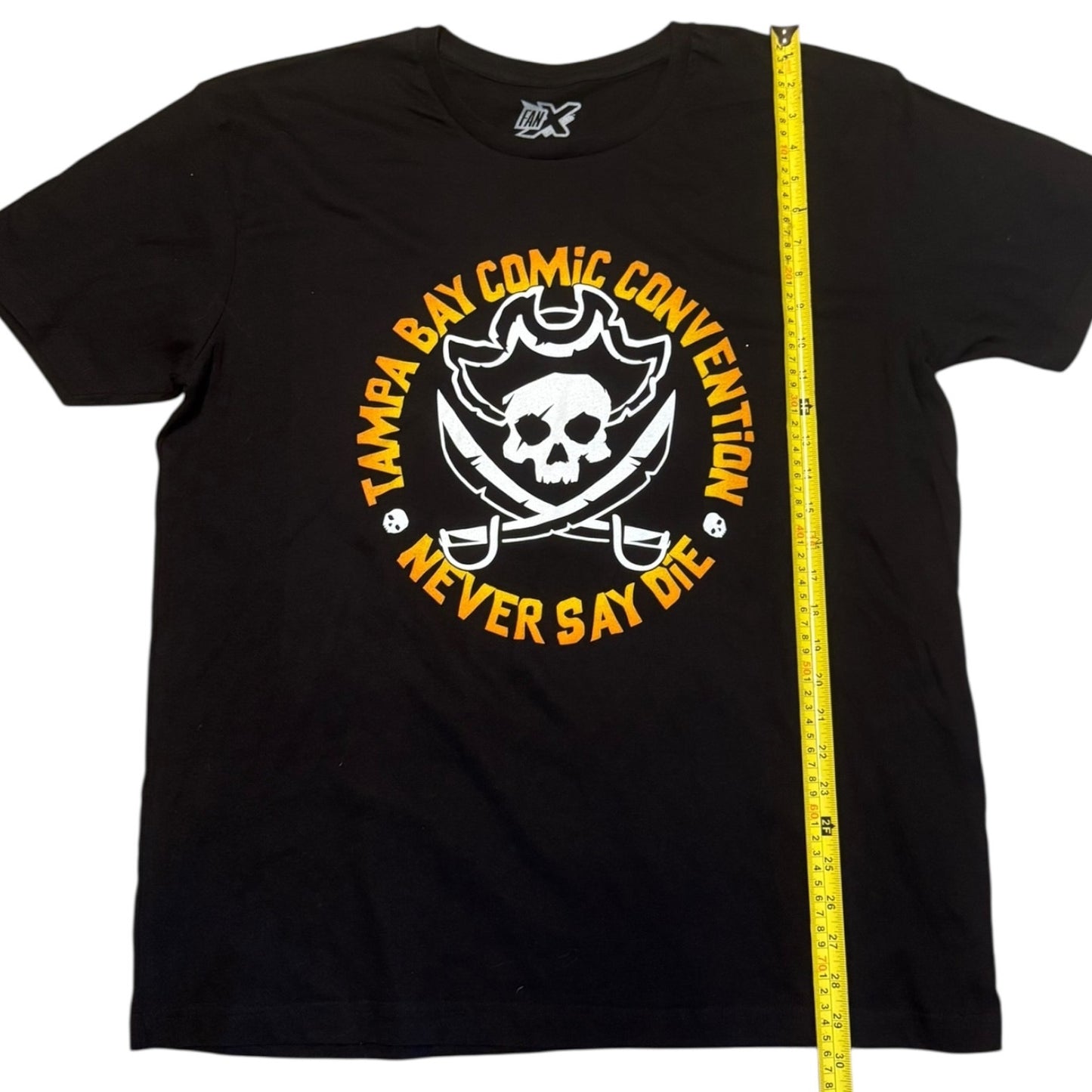 Black t-shirt with a skull and swords design and text, measured by a yellow tape measure.