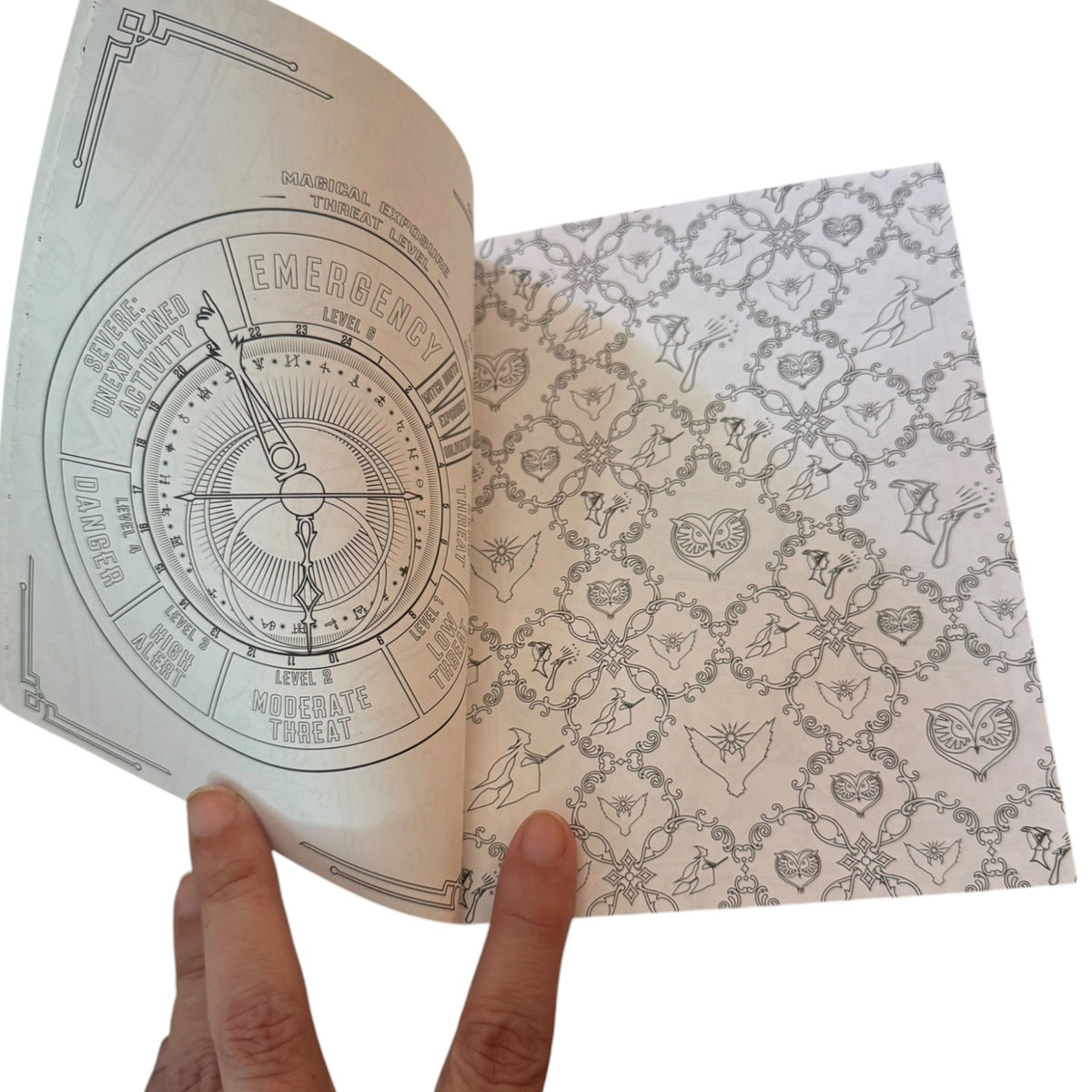An open coloring book showing printed pages, held by a person's fingers against a plain white background.