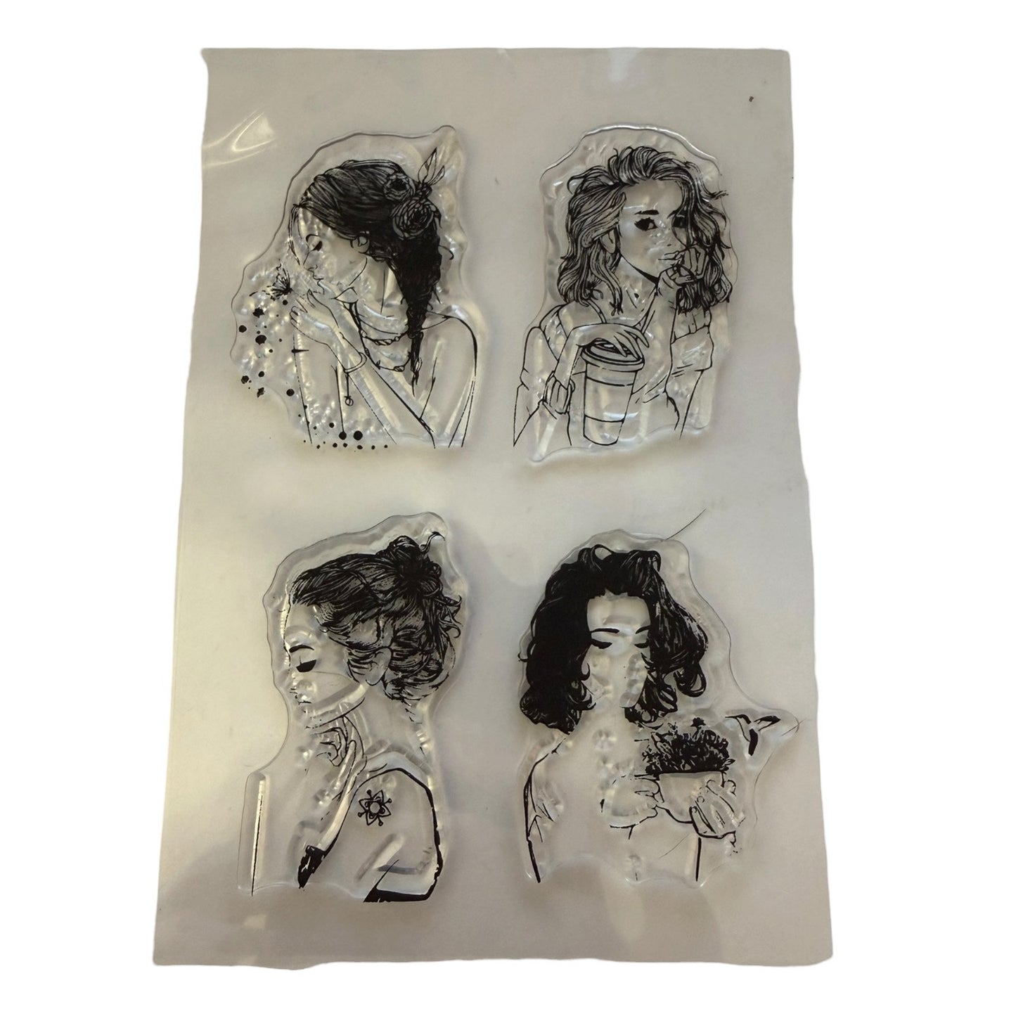 Four clear acrylic stamps featuring black ink sketches of women, displayed on a white backing sheet against a white background.