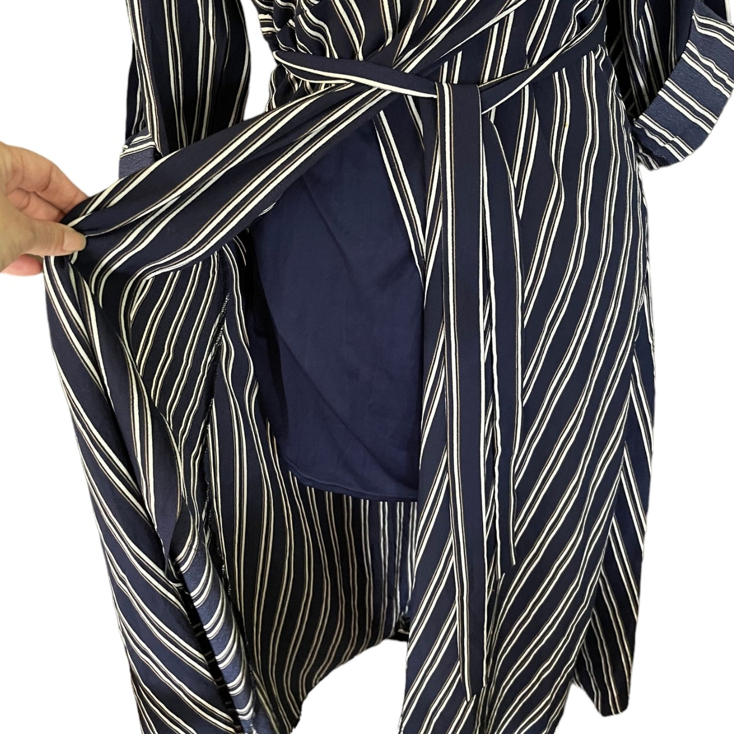 A close-up of a navy blue dress with white and blue diagonal stripes, featuring a hand holding open the front to reveal a solid navy blue lining.