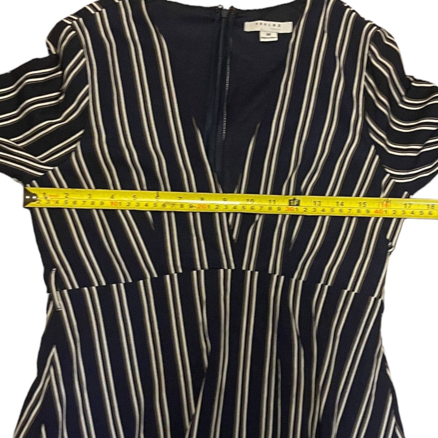 A short-sleeve striped dress with a front zipper, featuring vertical stripes on a white background, shown with a yellow tape measure across the chest.