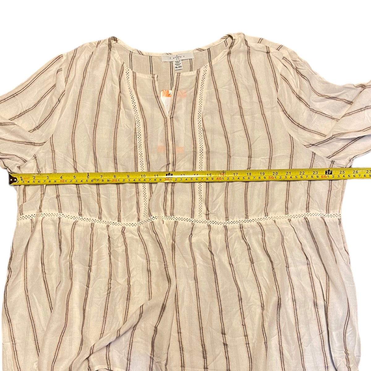 A cream-colored blouse with thin brown vertical stripes and lace trim, shown with a yellow tape measure across the chest to indicate width.