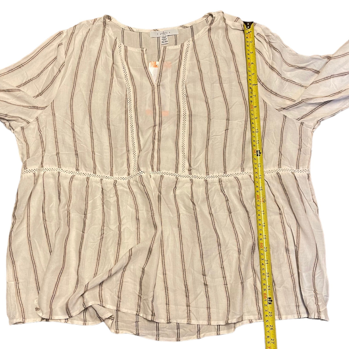 A cream blouse with thin brown vertical stripes and lace trim, laid flat on a white background with a yellow measuring tape running vertically to show the height.