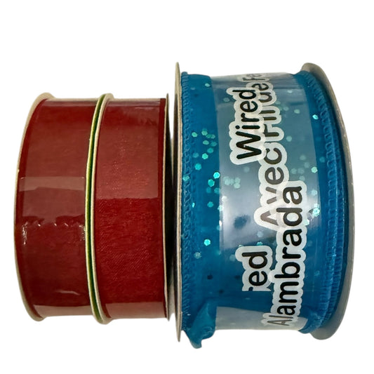 3 spools of decorative ribbon on a white background: two deep red ribbon and one blue glittery wired ribbon with white lettering.