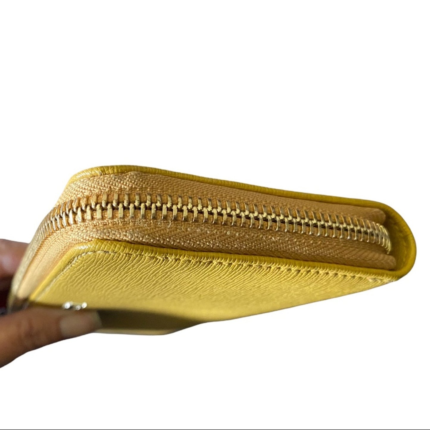 A close-up of a textured yellow leather zip-around wallet being held by a hand, showing the gold-toned zipper and leather grain against a white background.
