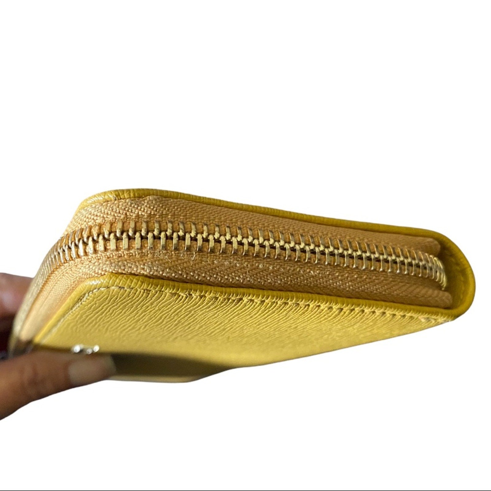 A close-up of a textured yellow leather zip-around wallet being held by a hand, showing the gold-toned zipper and leather grain against a white background.