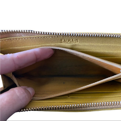 Close-up of a yellow wallet shown open, with a hand holding the zipper. The inside lining shows dirt and use, and the brand name 'FURLA' is embossed near the top.