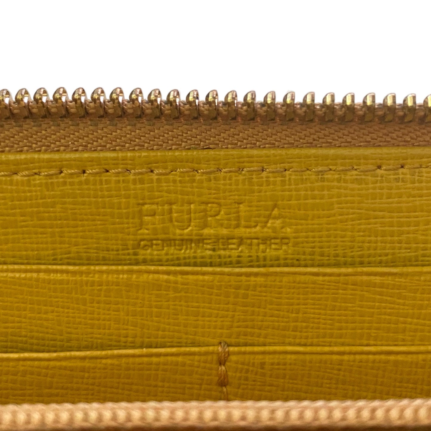 Close-up of a Furla leather zippered wallet , showing the embossed Furla logo on the interior, a textured mustard-yellow leather surface, and gold-toned metal zippers.