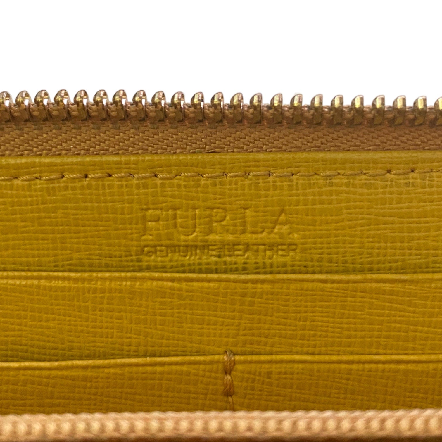 Close-up of a Furla leather zippered wallet , showing the embossed Furla logo on the interior, a textured mustard-yellow leather surface, and gold-toned metal zippers.