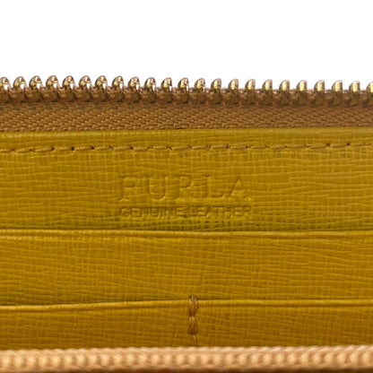 Close-up of a Furla leather zippered wallet , showing the embossed Furla logo on the interior, a textured mustard-yellow leather surface, and gold-toned metal zippers.