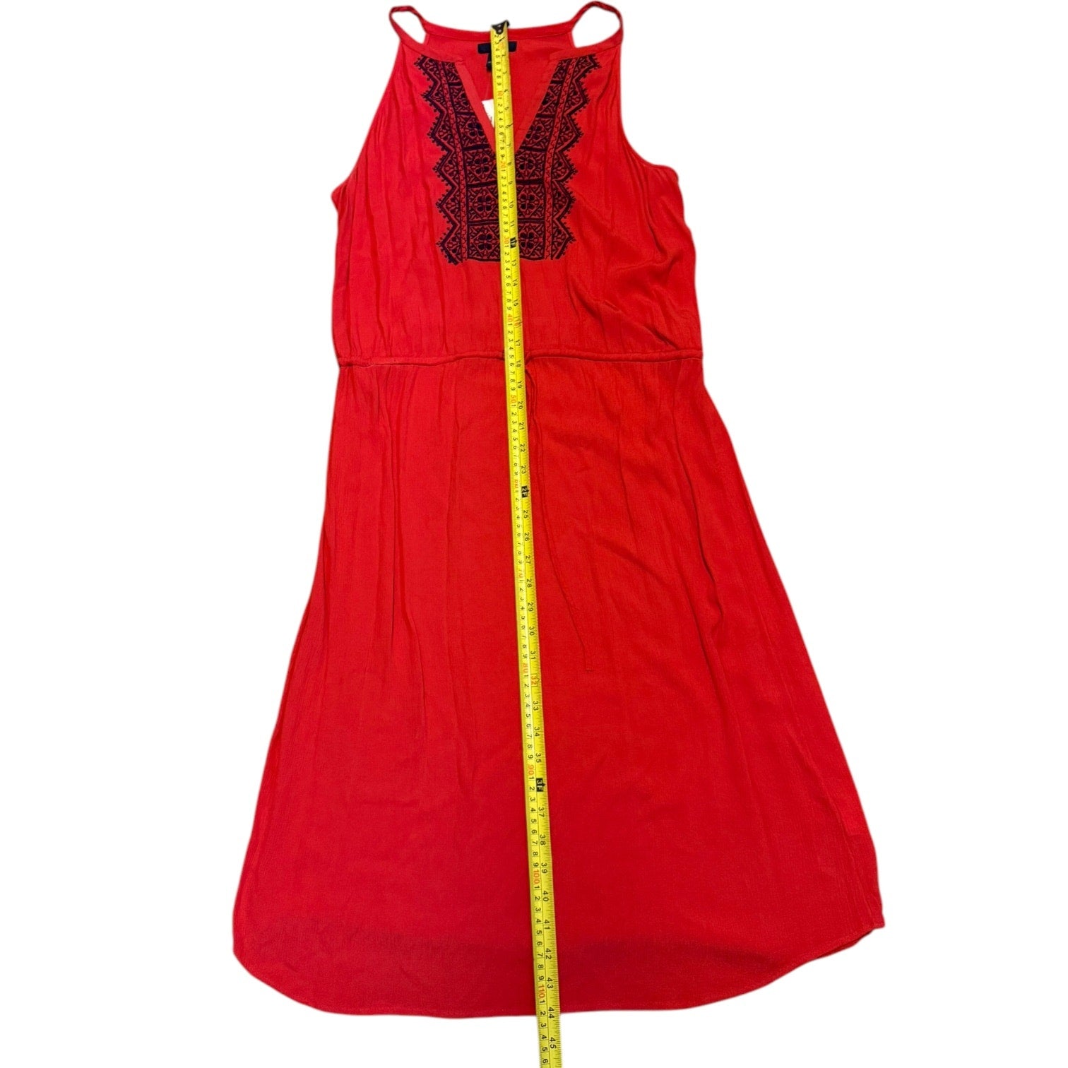 Red dress with blue embroidery and a tape measure for size reference on a white background