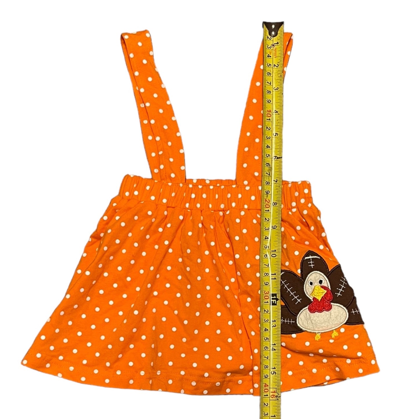 Orange dress with white polka dots and a turkey design, measured by a tape measure on a white background.