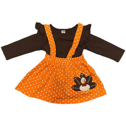 Front of girl's outfit with brown long-sleeve shirt and orange polka dot dress with turkey applique on a white background