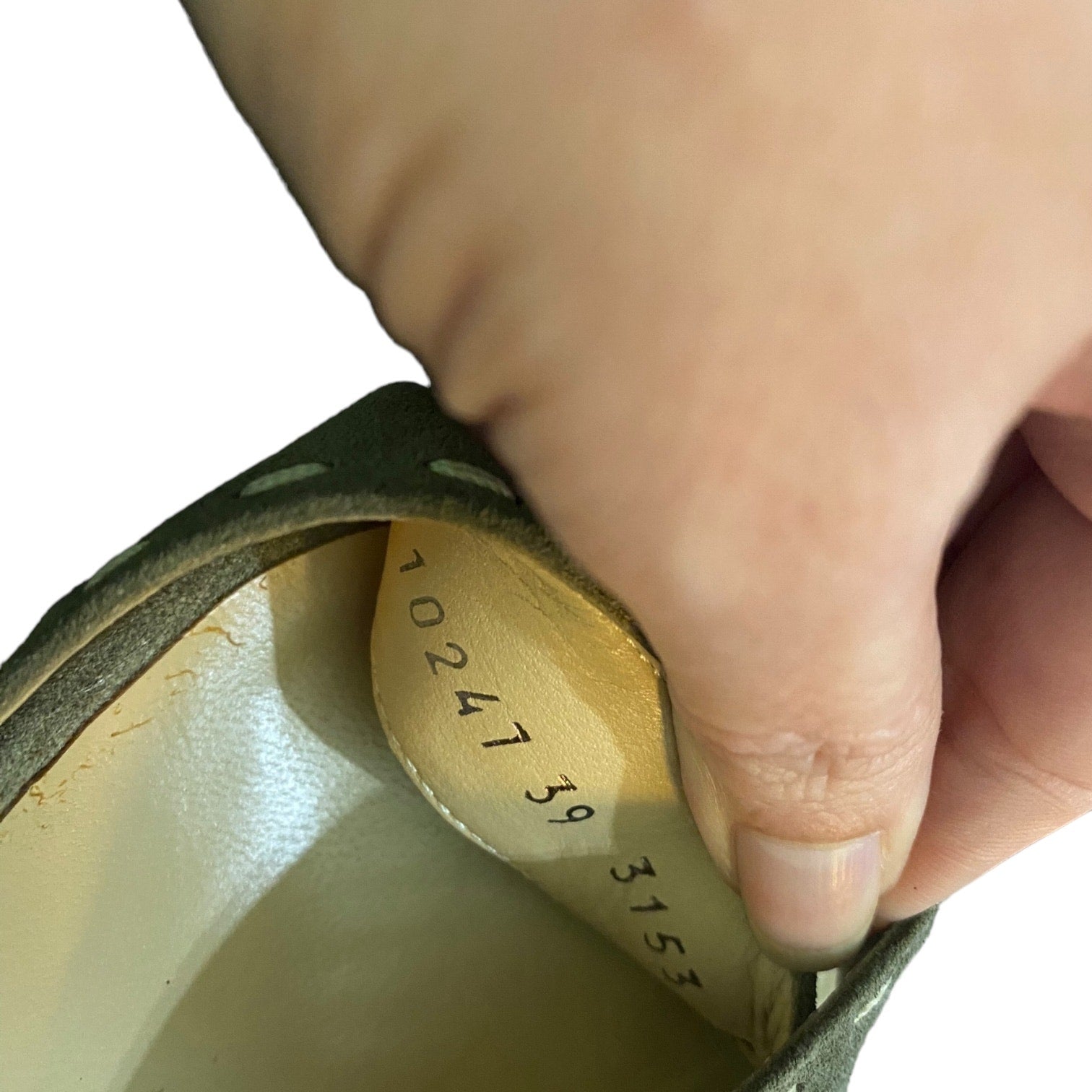 Close-up of a hand holding a shoe with a visible serial number on a white background