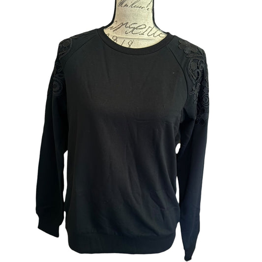 A black crewneck sweatshirt displayed on a vintage-style mannequin torso. The sweatshirt features black floral lace applique detailing on the shoulders.
