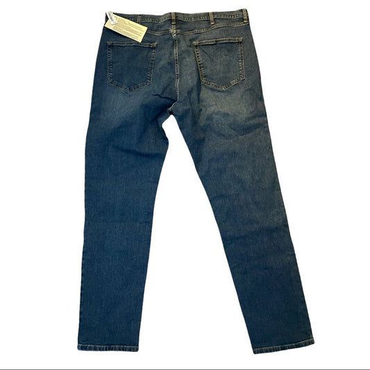 A pair of dark blue denim jeans shown from the back, featuring a standard five-pocket design and a light-colored paper tag attached to the waistband, set against a plain white background.