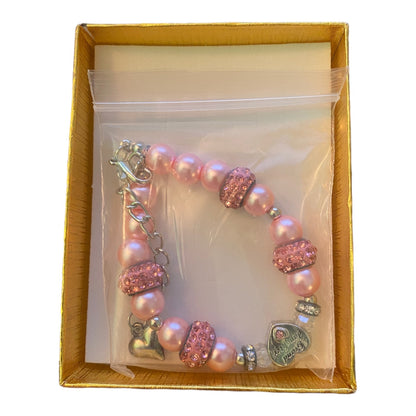 A pink beaded bracelet with rhinestone-embellished beads, a silver lobster clasp, and heart charms, presented inside a clear plastic bag and a gold gift box.