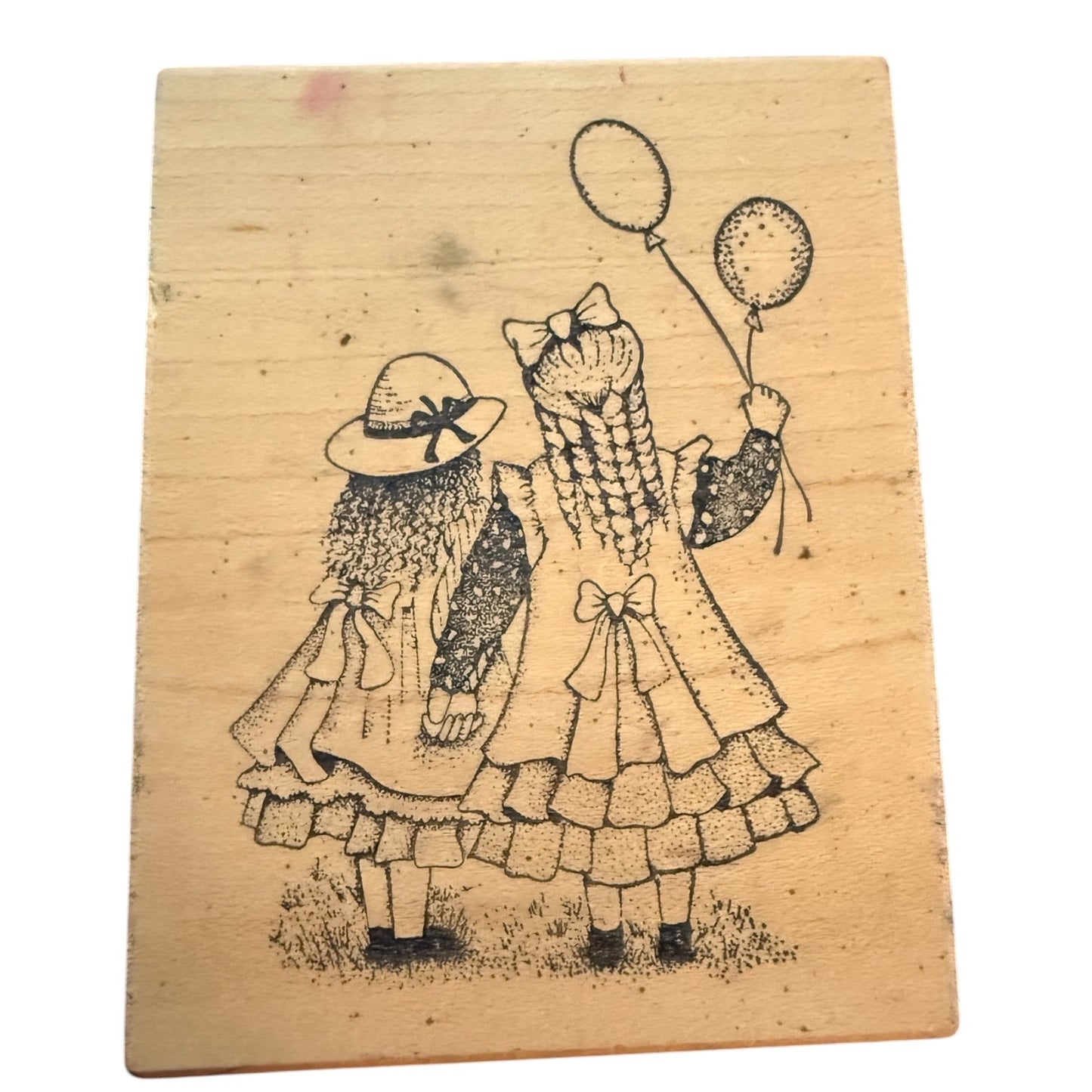 Wooden block with a black ink drawing of two girls in dresses and hats on a white background.