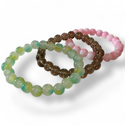 Set of three beaded bracelets in green, smoke, and pink on a white background