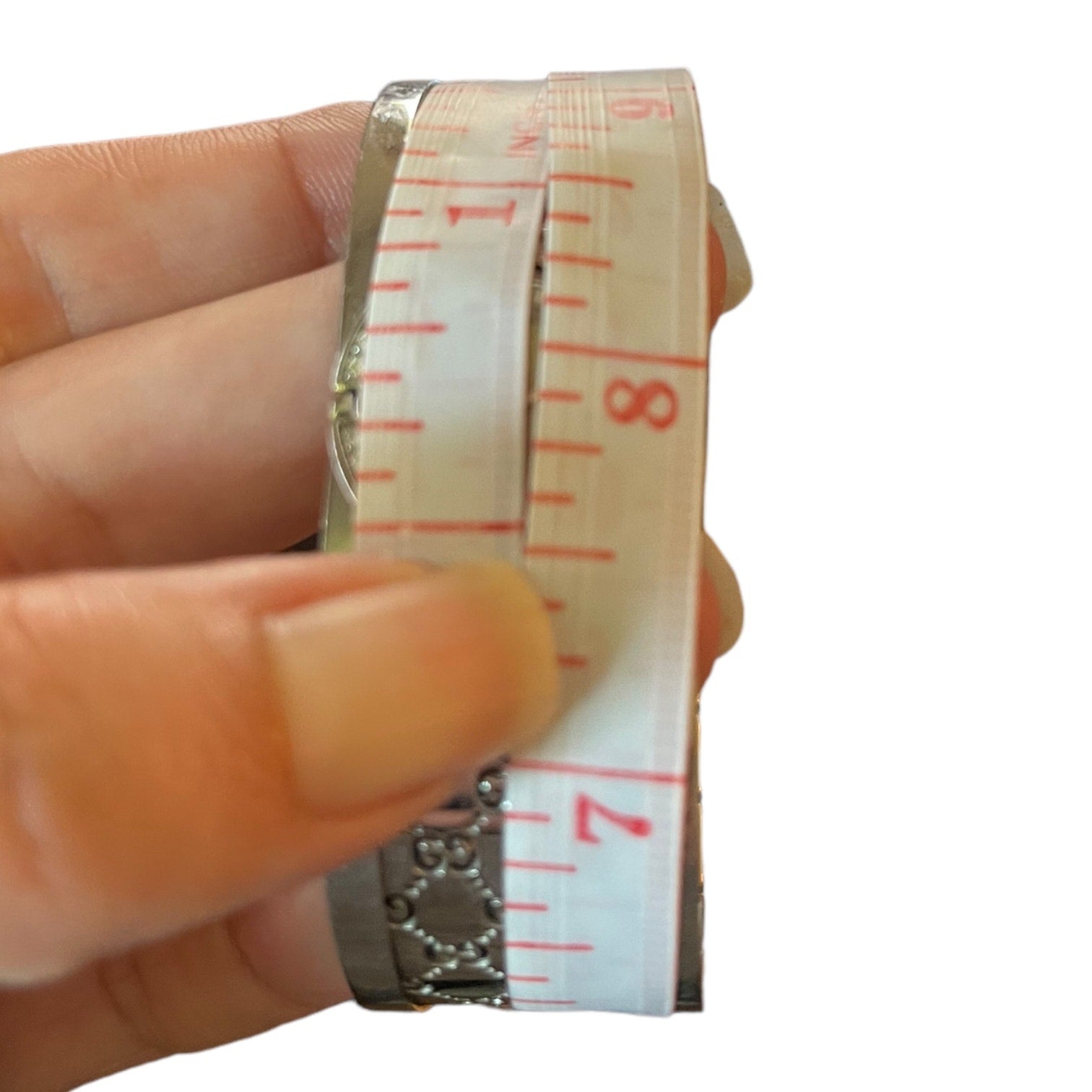 Hand holding a measuring tape with red markings on a white background