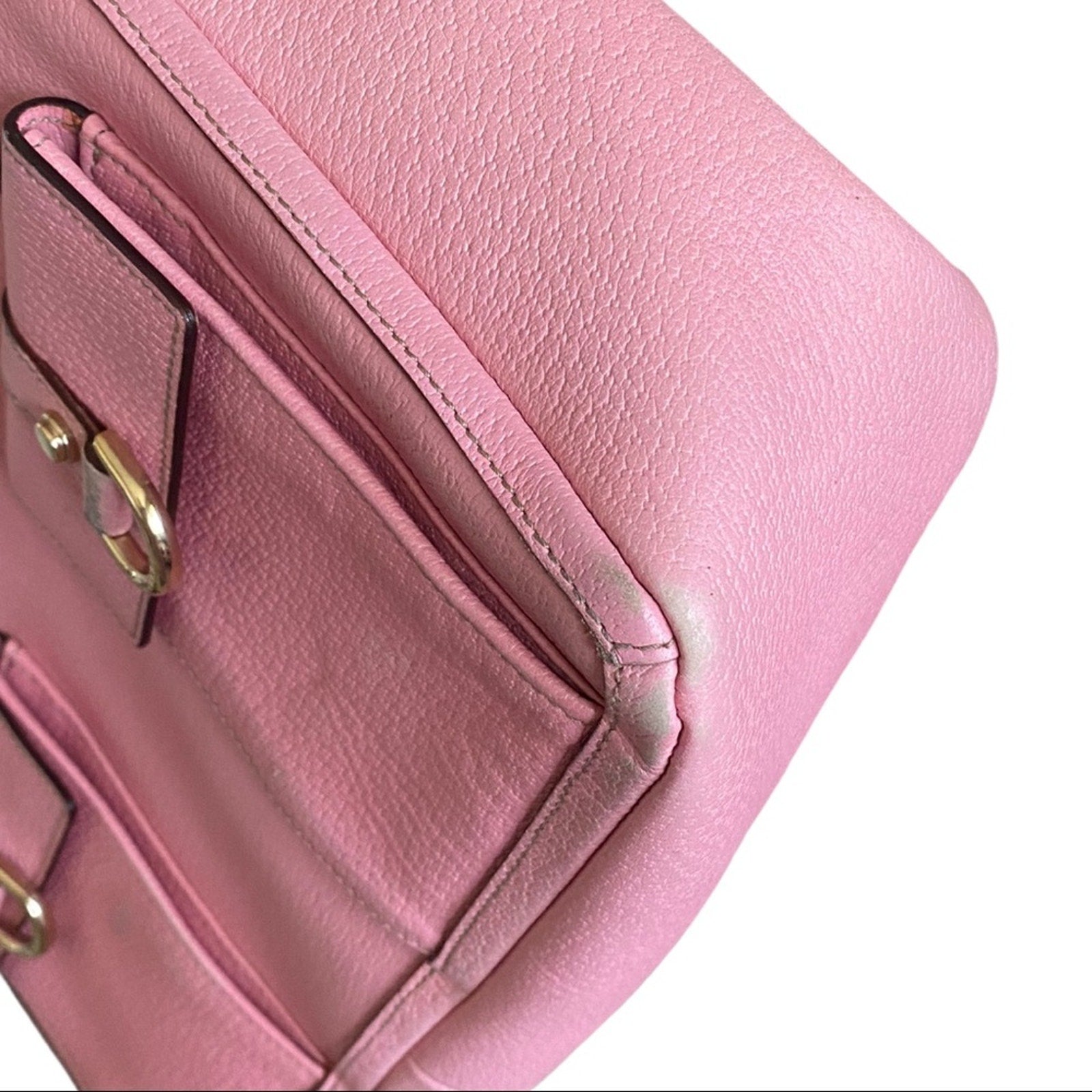 Close-up of a pink handbag corner with gold hardware on a white background