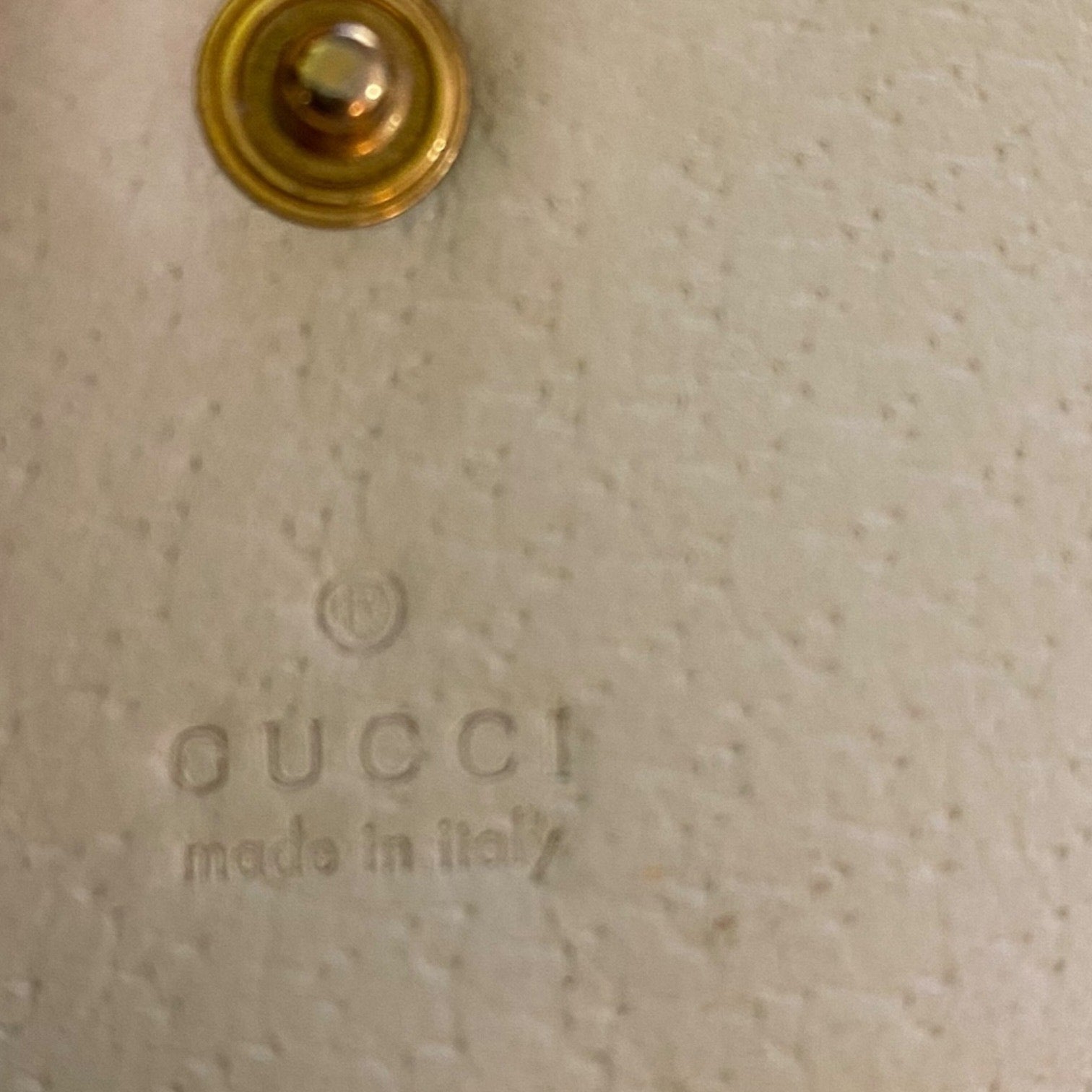Close-up of Gucci logo on a beige textured surface with a gold circular detail.
