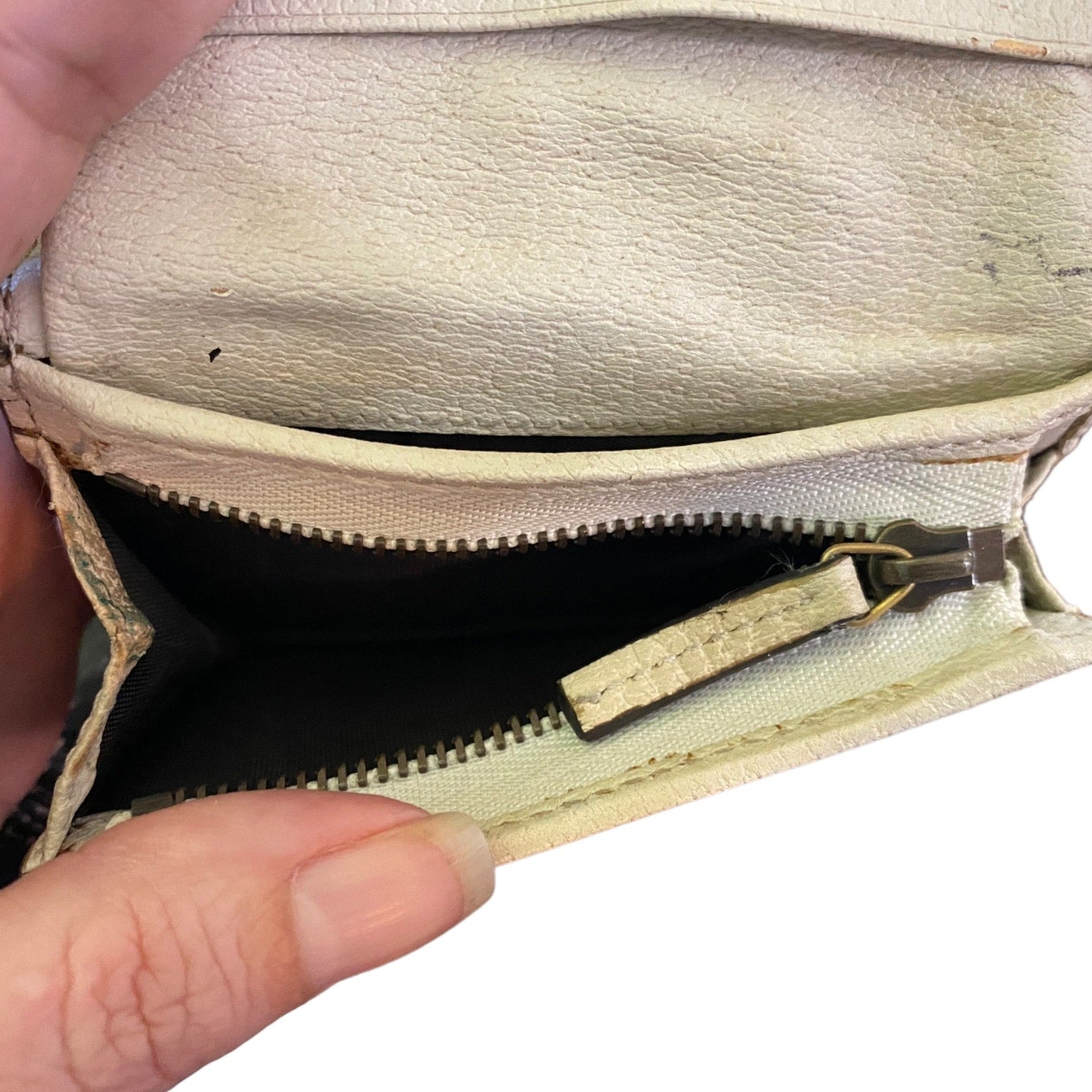 Beige leather wallet with a zipper held open by a hand on a white background