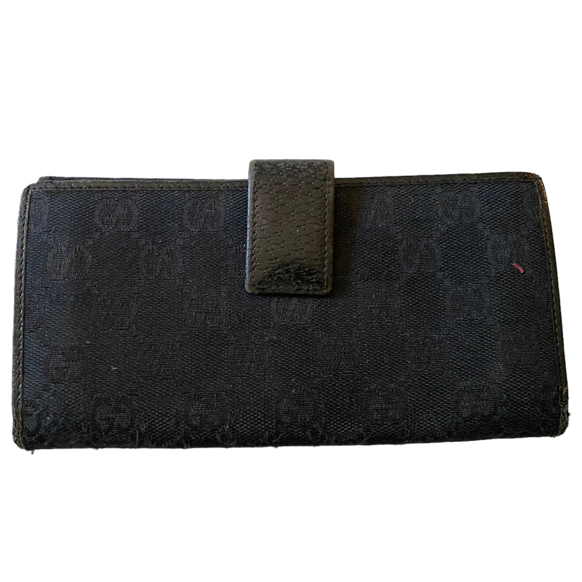 A black Gucci long wallet featuring the brand's signature GG monogram canvas and a textured black leather tab closure on the front, set against a plain white background.