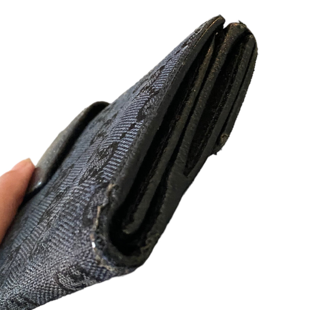 A close-up of a black textured wallet held by a hand, showing the edges and scuffing and the side of the wallet against a plain white background.