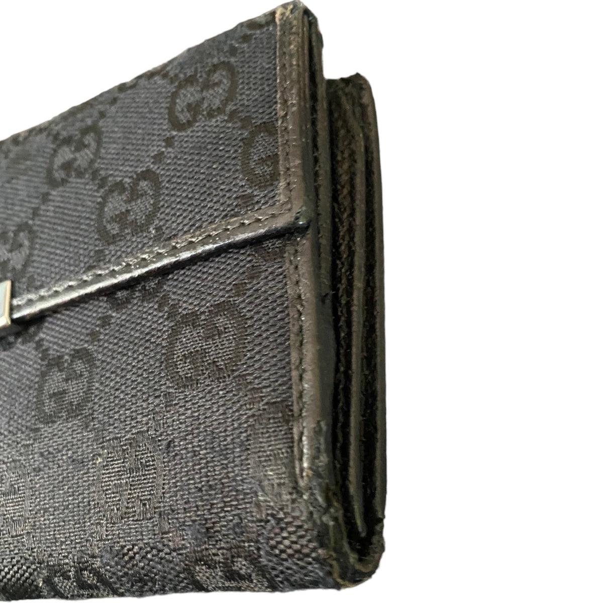 Close-up of a black monogram canvas wallet showing the textured pattern and leather trim with scuffs on a white background.