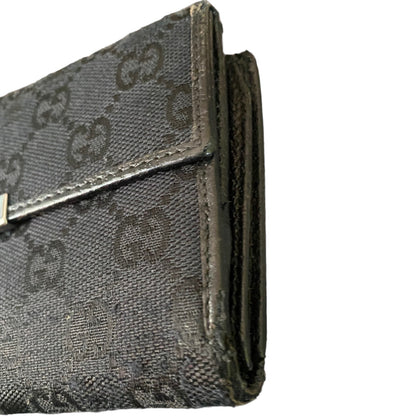 Close-up of a black monogram canvas wallet showing the textured pattern and leather trim with scuffs on a white background.