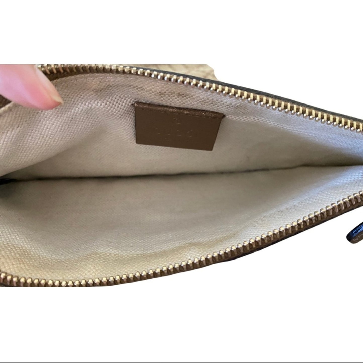 Close-up of a beige pouch with a gold zipper and visible brand logo on a white background.