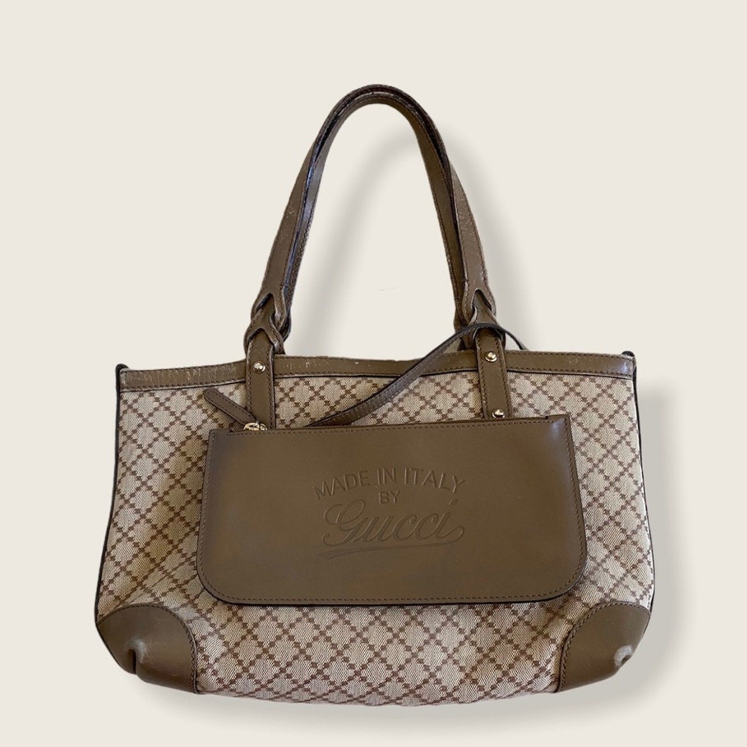 Brown handbag with patterned design and 'Made in Italy by Gucci' text on a beige background