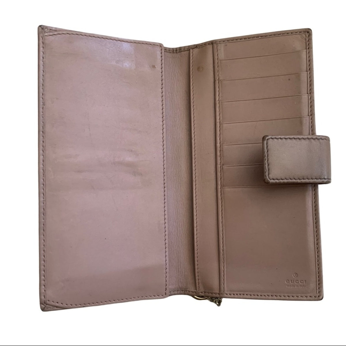 An open Gucci leather wallet showing its interior compartments, card slots, and a small embossed Gucci logo on the lower right.