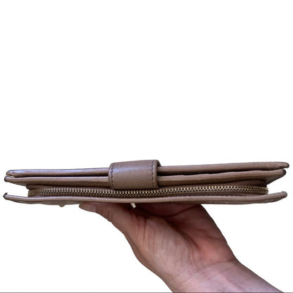 Hand holding a pink leather wallet against a white background showing top edges