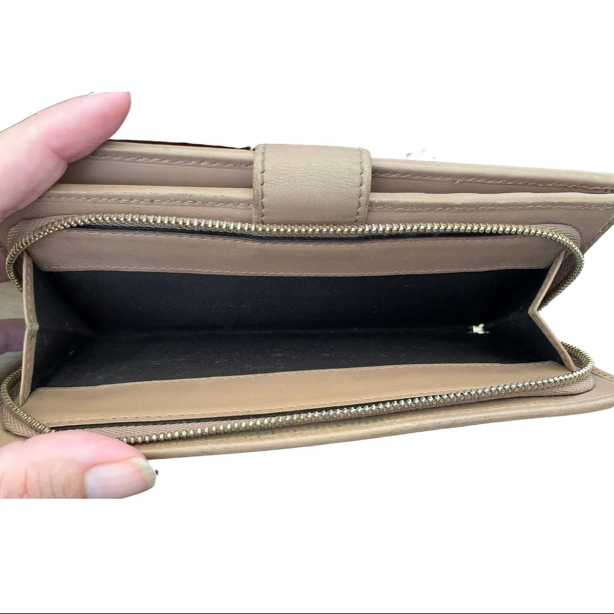 A pink leather wallet shown open, held by a hand, displaying its interior compartments and black lining against a white background.