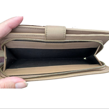 A pink leather wallet shown open, held by a hand, displaying its interior compartments and black lining against a white background.