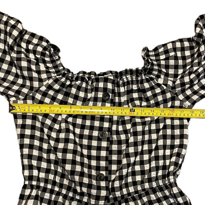Black and white gingham check top with  a yellow measuring tape stretched horizontally across the chest to show the width.
