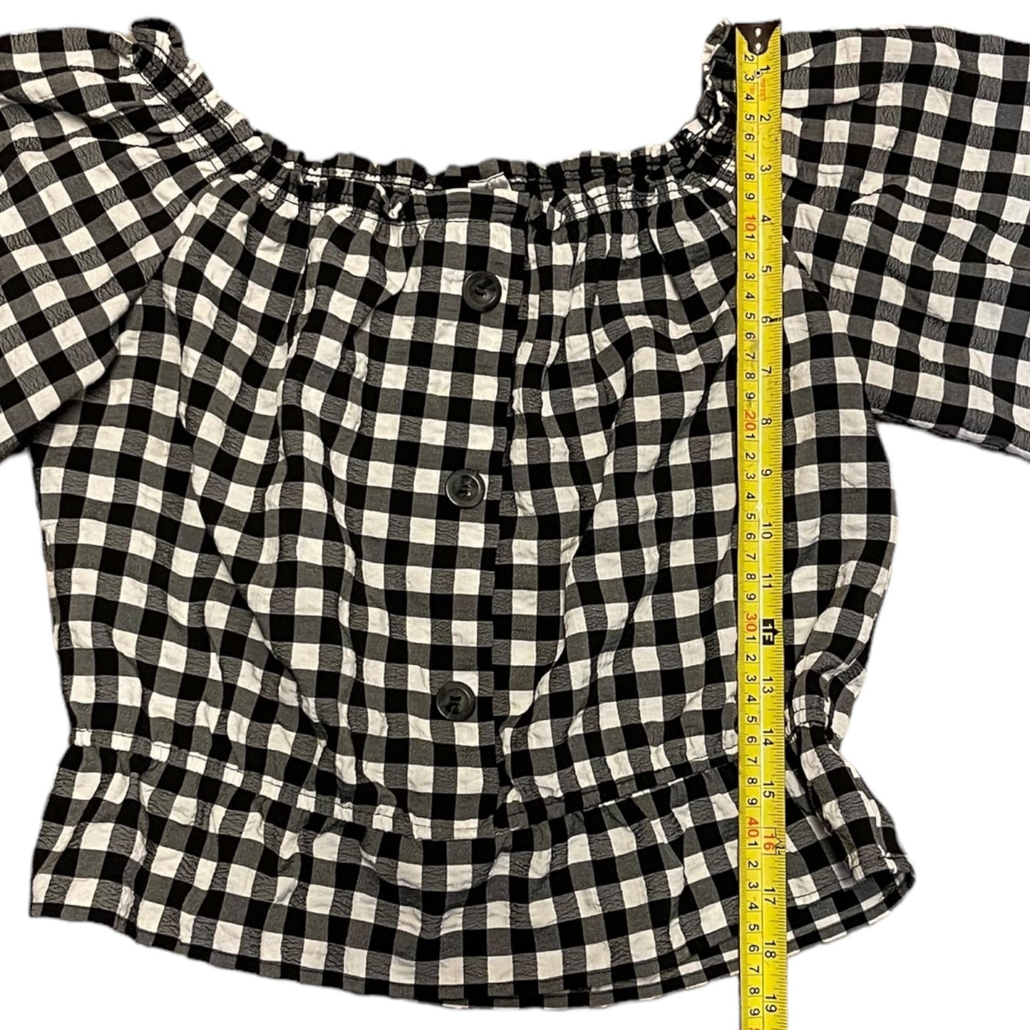 A black and white gingham check  with a button-down front, shown with a yellow tape measure on a white background.