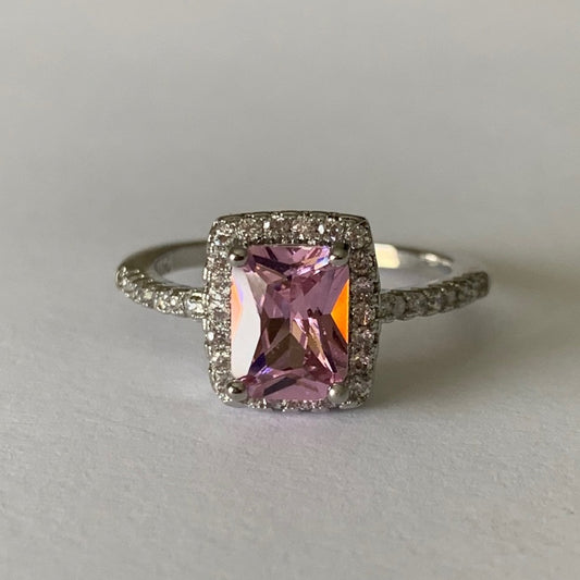 Ring with a pink gemstone and diamond-studded band on a light gray background