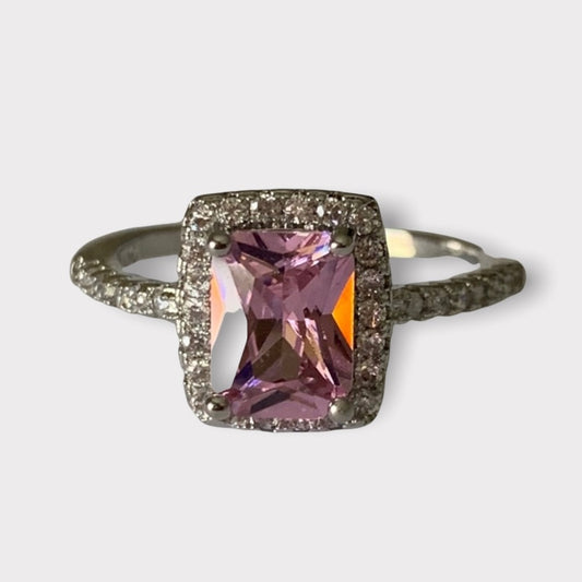 Ring with a pink gemstone and diamond-studded band on a light gray background