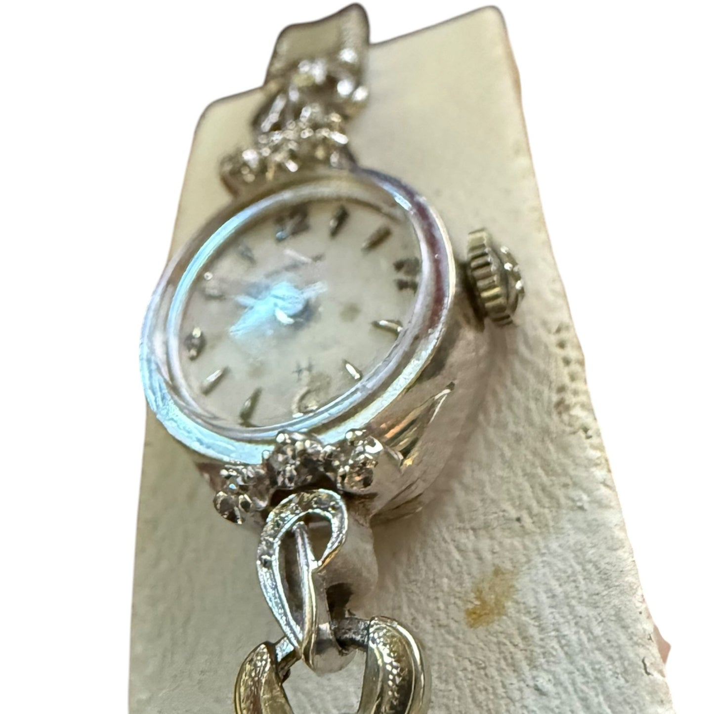 Decorative silver white gold watch with intricate designs on a textured beige background