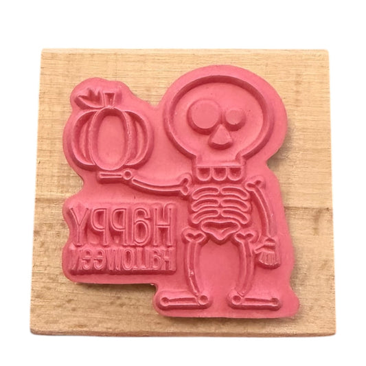 Pink skeleton rubber stamp with 'Happy Halloween' text on a wooden block