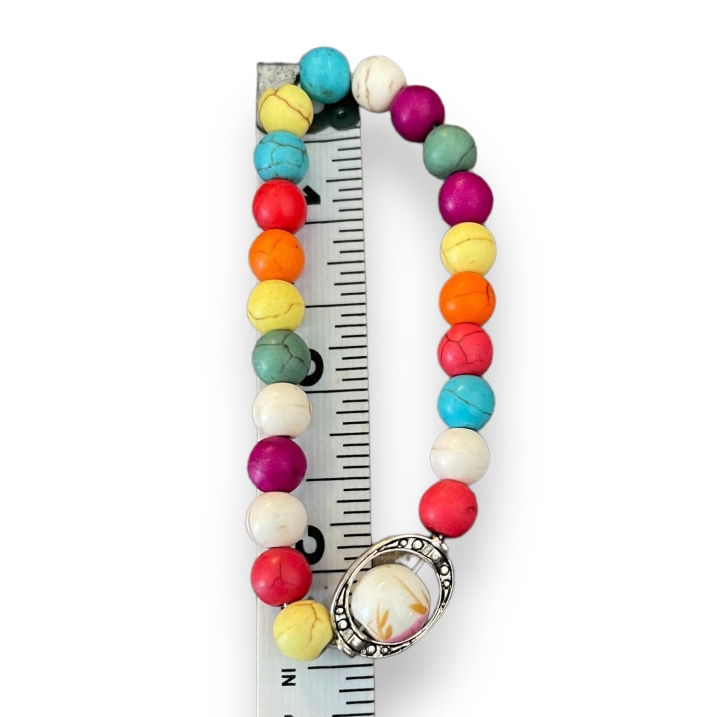 Colorful beaded bracelet with a silver charm on a ruler for size reference