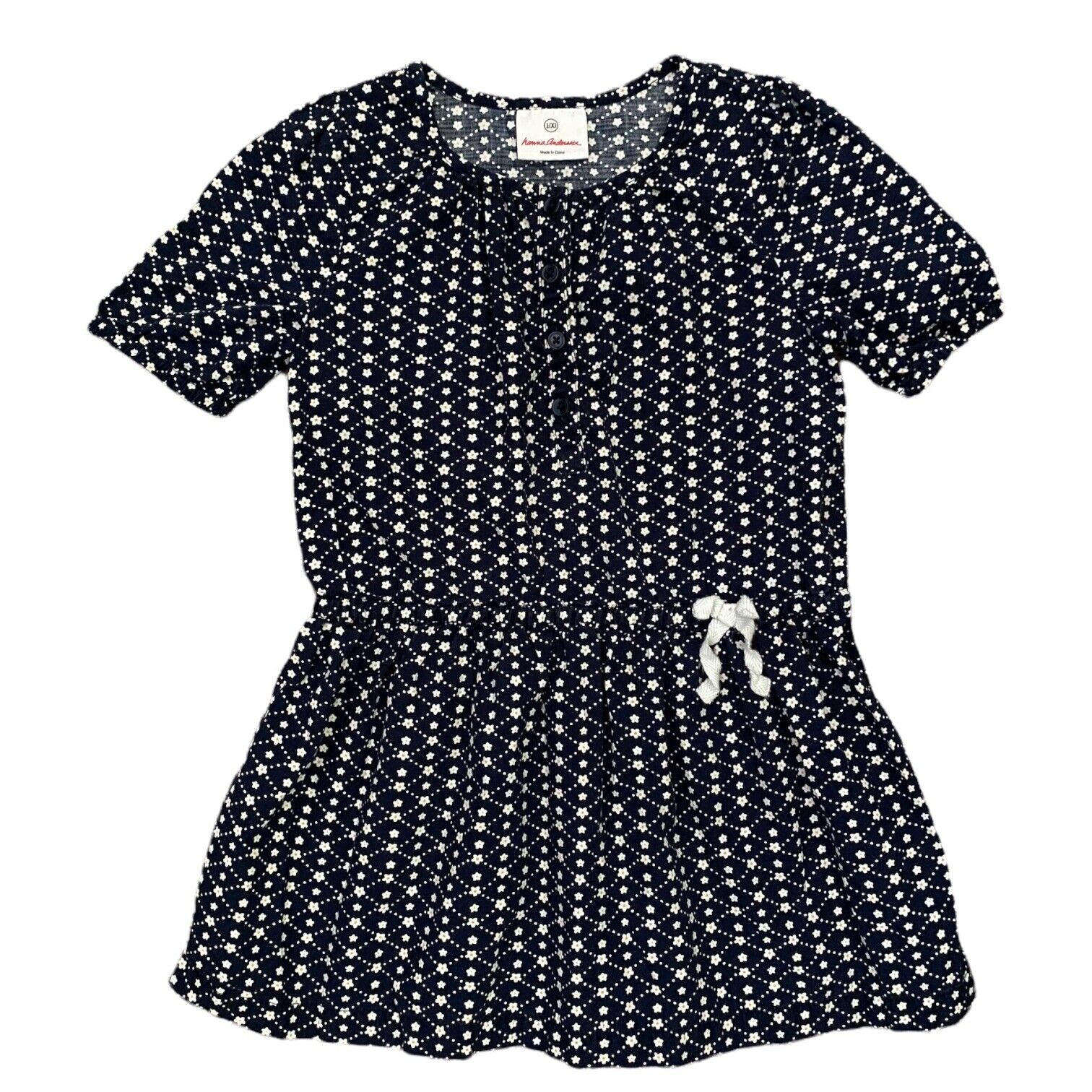 A short-sleeve peplum-style dress with an allover white floral print on a dark navy background, featuring a gathered waist and a small white bow detail on the front.
