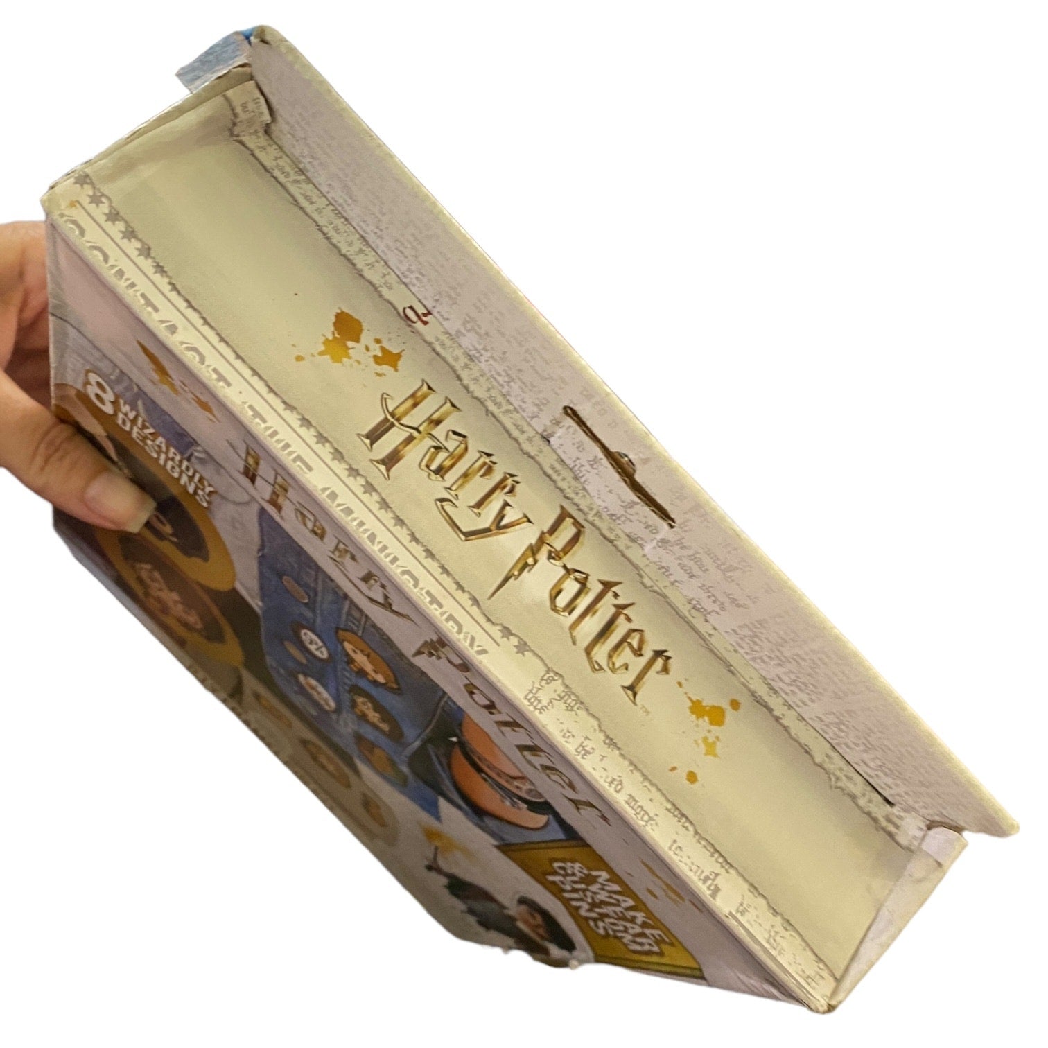 Harry Potter-themed box held by a hand  showing damage on a white background